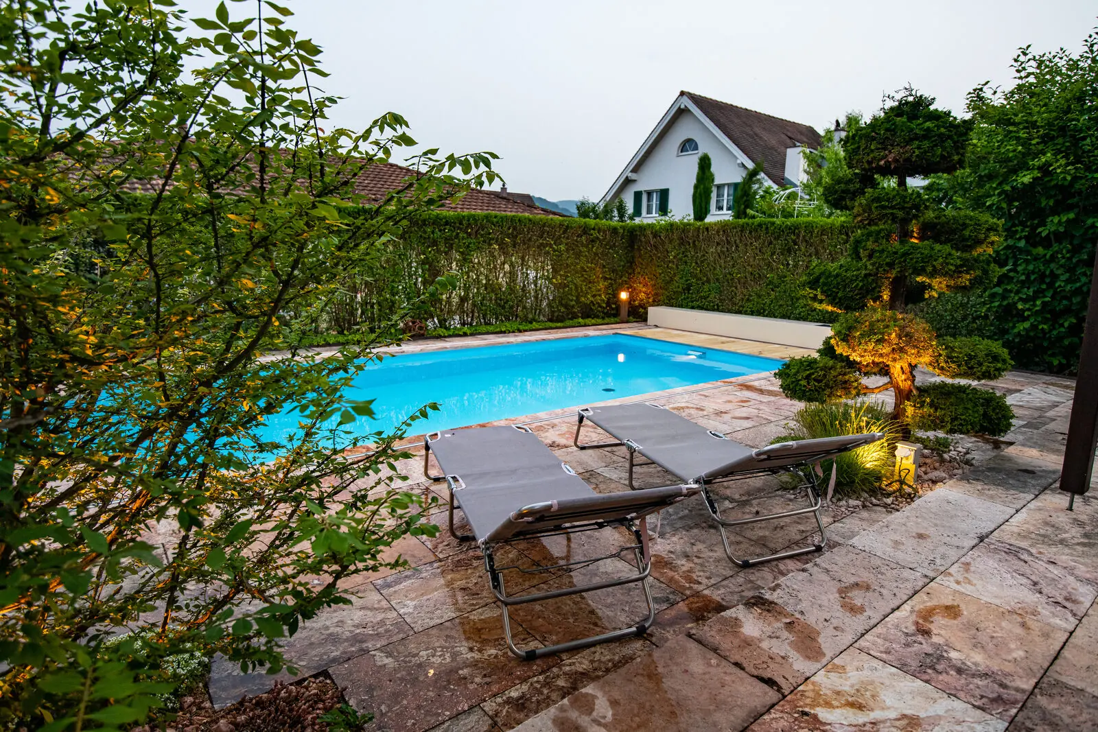 A covered pool at dusk, garden lights glowing — the evening at peace